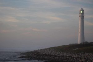 picture of white lighthouse, ocean, and cloudy sky
