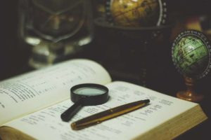 Picture of magnifying glass and pen on book surrounded by globes